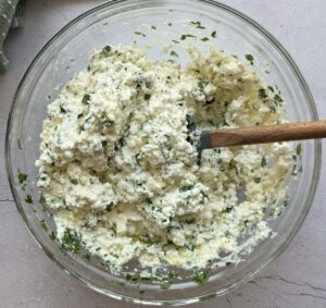 bowl of ricotta mixed with parmesan and chopped parsley, spatula in the bowl