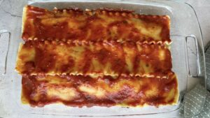layer of tomato sauce on top of lasagna noodles in a glass baking dish