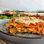 slice of lasagna with beef and ricotta on a plate garnished with fresh parm and parsley, another slice on a plate in the background