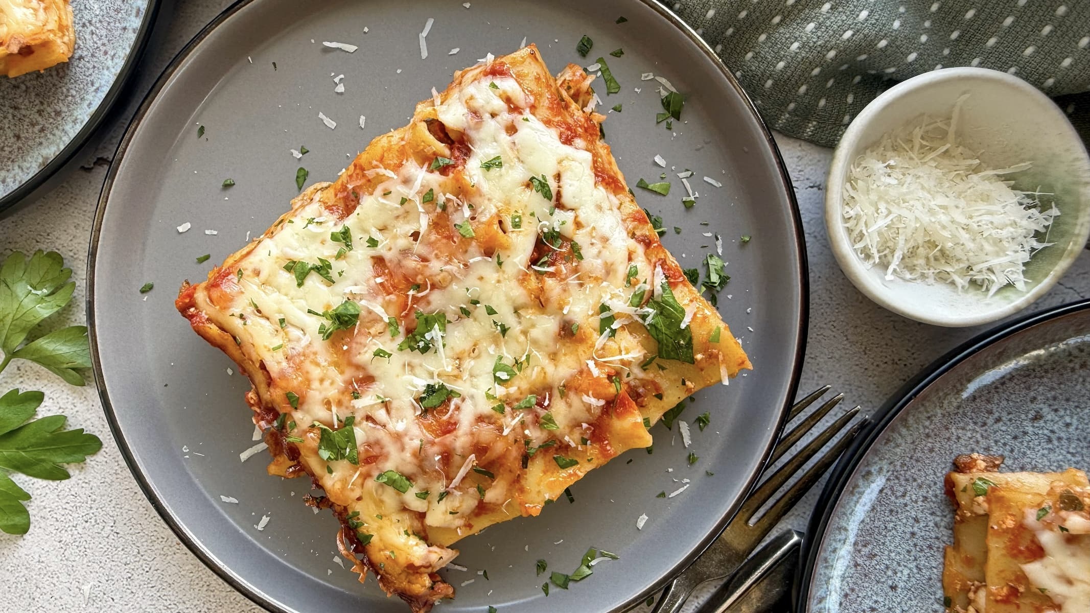 slice of cheesy lasagna on a plate with fresh parm and parsley