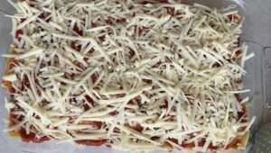 uncooked lasagna with a layer of grated mozzarella cheese on top
