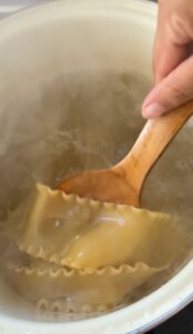 hand with a wooden spoon in a pot of boiling lasagna noodles