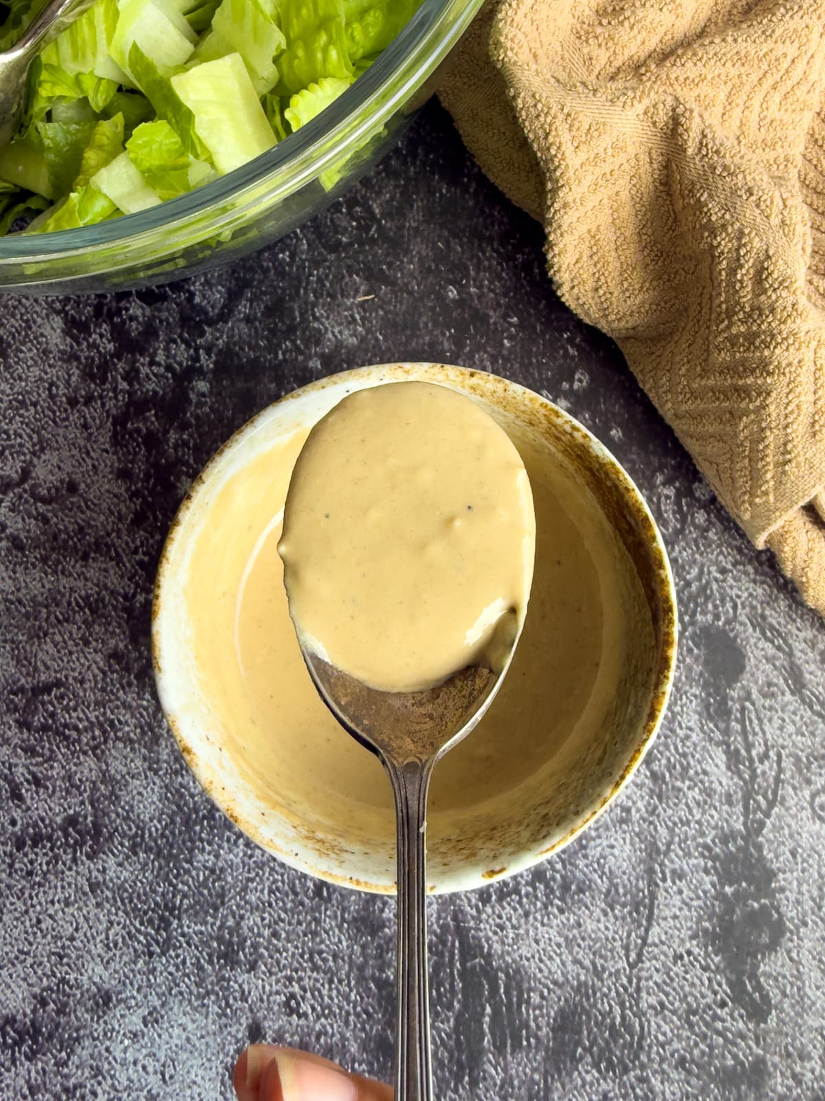 spoonful of caesar dressing over a bowl with more, next to a bowl of chopped lettuce