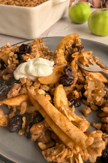 apple cranberry crisp on a plate with greek yogurt, oats and dried cranberries, dish with more in the background next to 2 apples