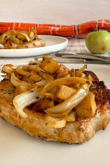 apples and onions on top of a cooked pork chop, another in the background next to an apple