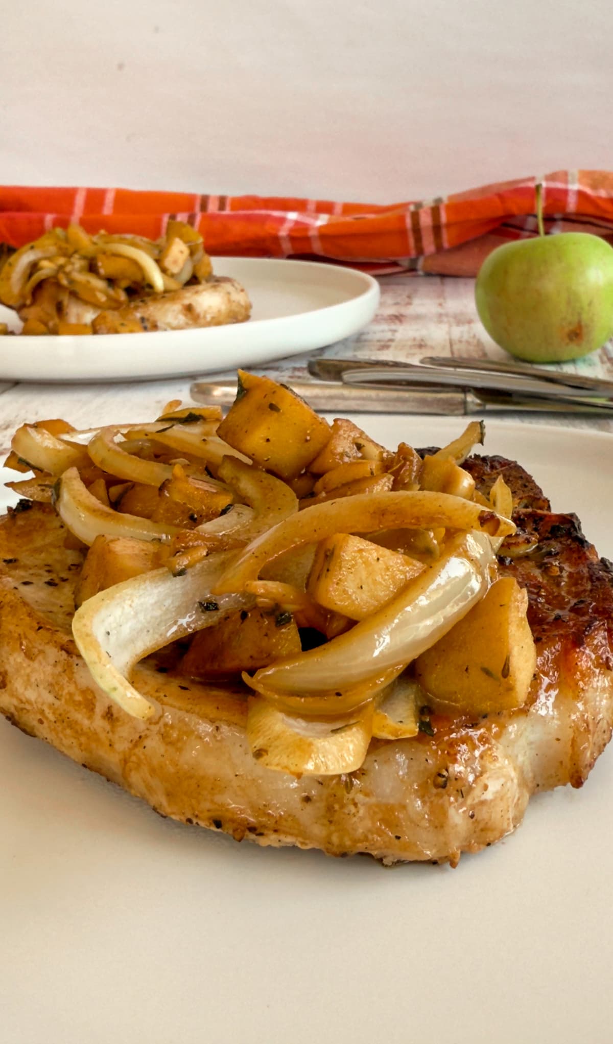apples and onions on top of a cooked pork chop, another in the background next to an apple