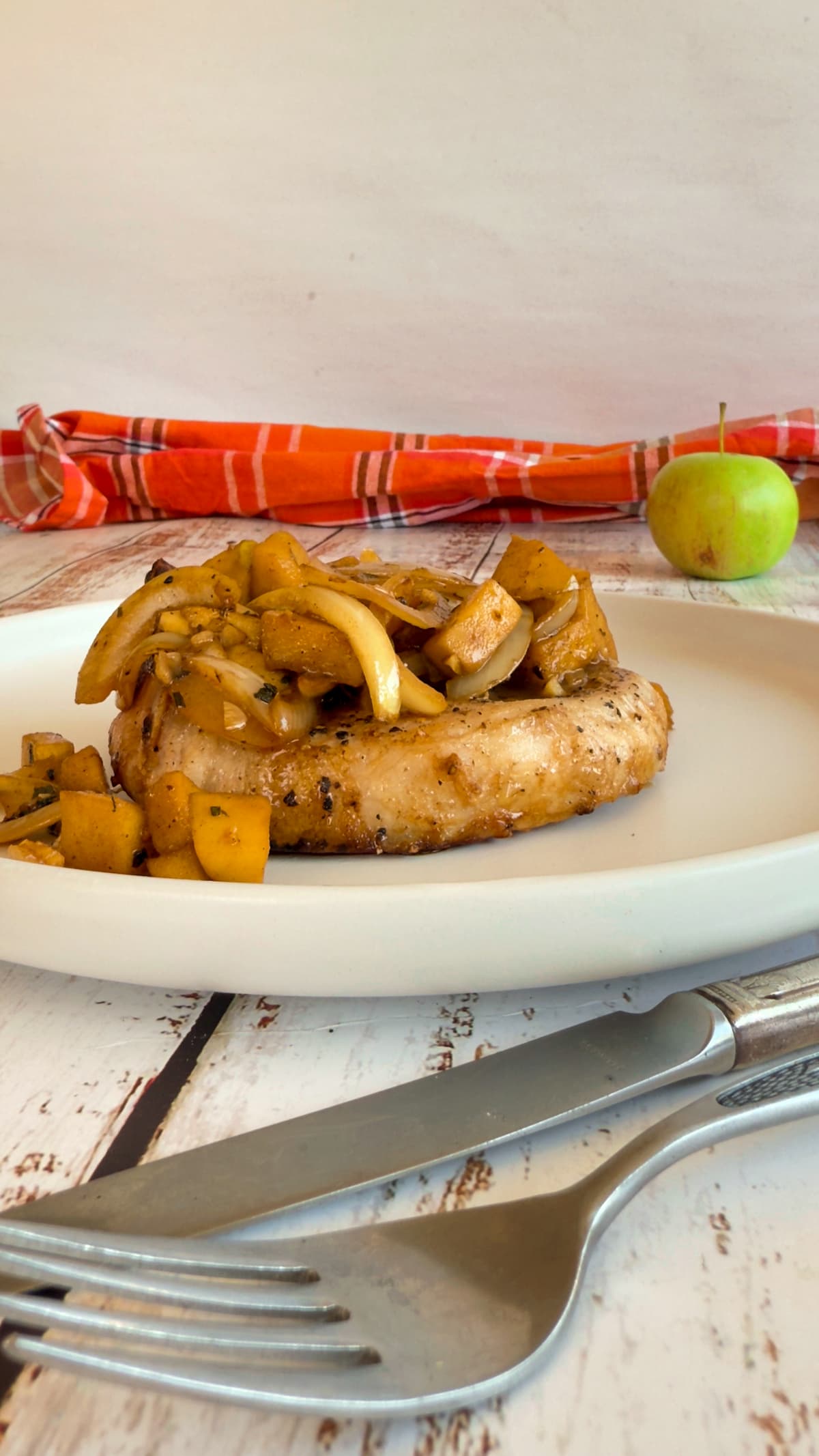 pork chop on a plate with sauteed apples and onions, apple in the background