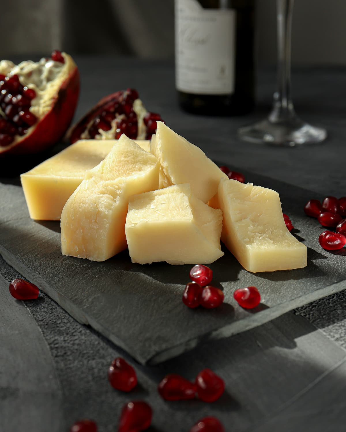 small blocks of parmesan cheese on a board with pomegranate seeds