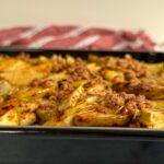 sliced apples on a sheet tray topped with caramel sauce and granola crumble