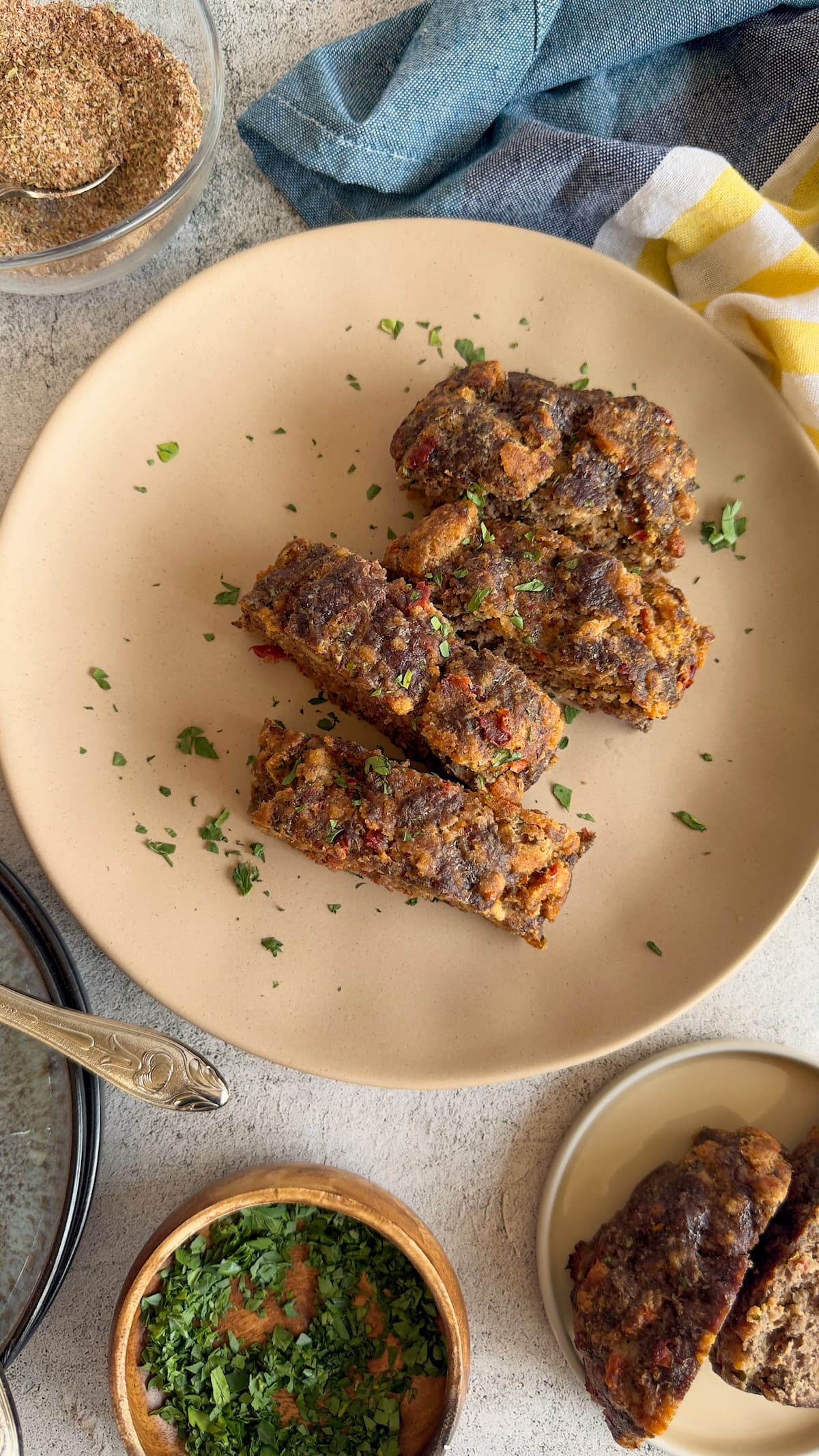 sliced meatloaf on a plate surrounded by bowl of chopped parsley, meatloaf seasoning, and more meatloaf