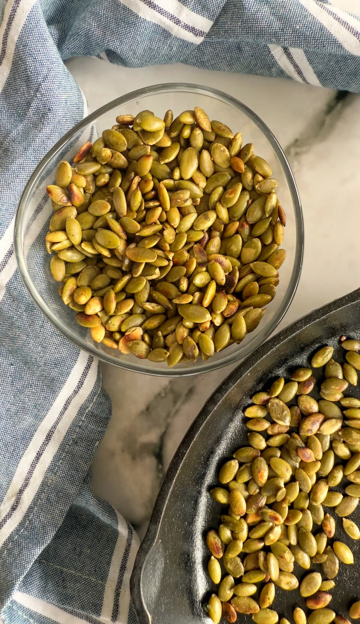 bowl of toasted pumpkin seeds next to a cast iron skillet with more