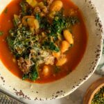 bowl of soup with kale, white beans, celery, parmesan in a tomato broth