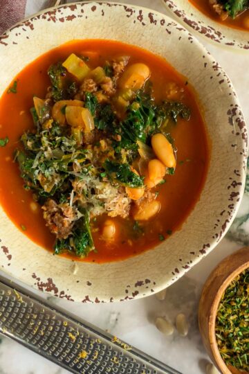 bowl of soup with kale, white beans, celery, parmesan in a tomato broth