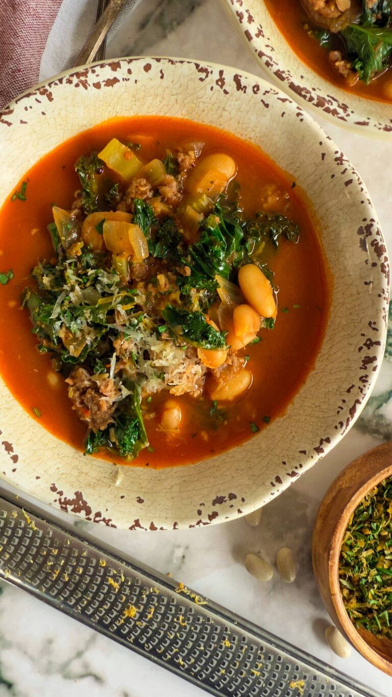 bowl of soup with kale, white beans, celery, parmesan in a tomato broth