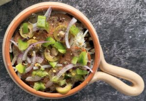 uncooked cottage cheese pizza bowl with sliced red onions, pepperoni, green pepper, green olives, cheese and seasoning
