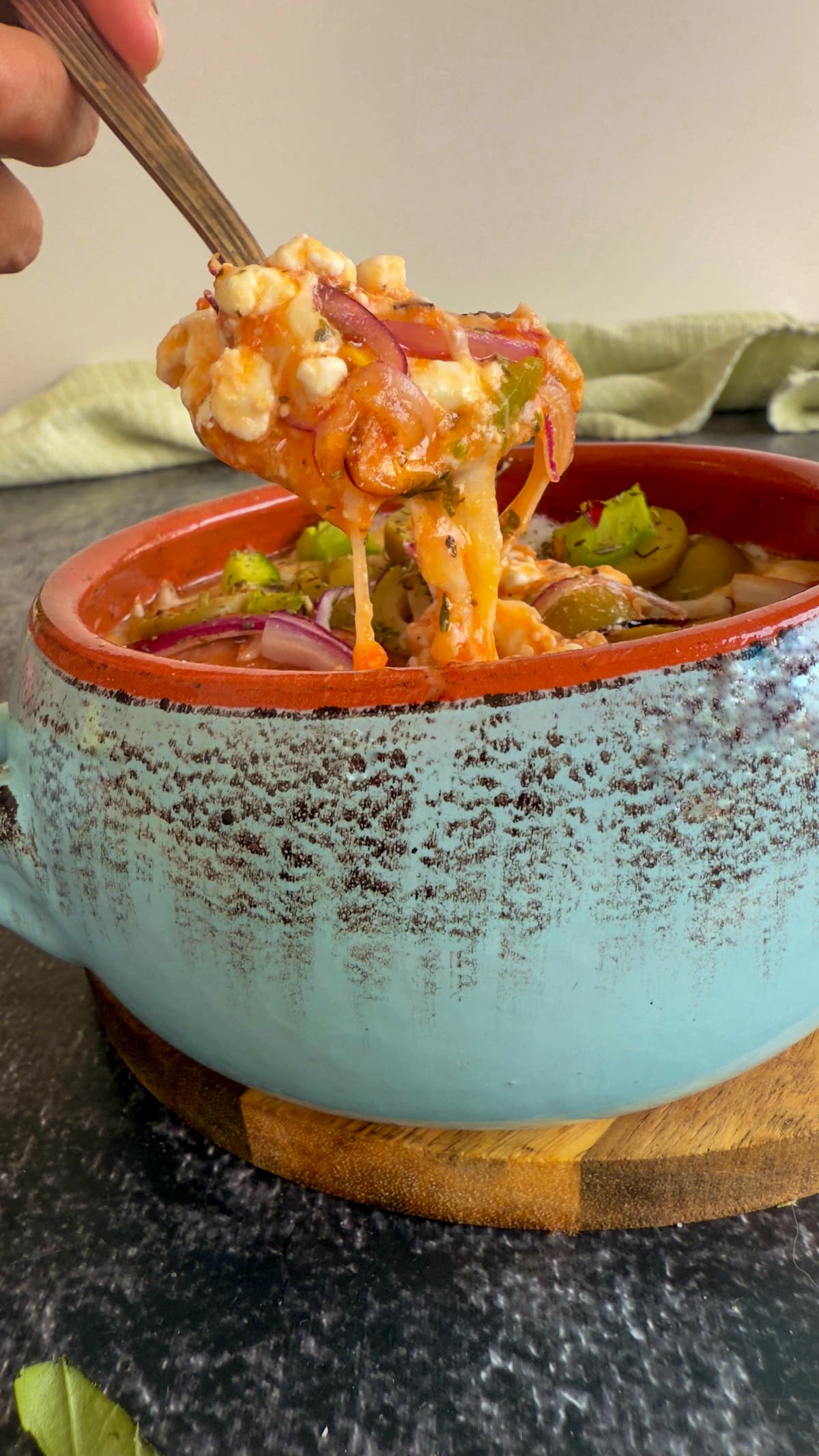 hand with a spoon pulling out of a cottage cheese pizza bowl showcasing a melty cheese pull