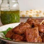 plate of cooked steak bites with jar of chimichurri in the background