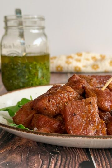 plate of cooked steak bites with jar of chimichurri in the background