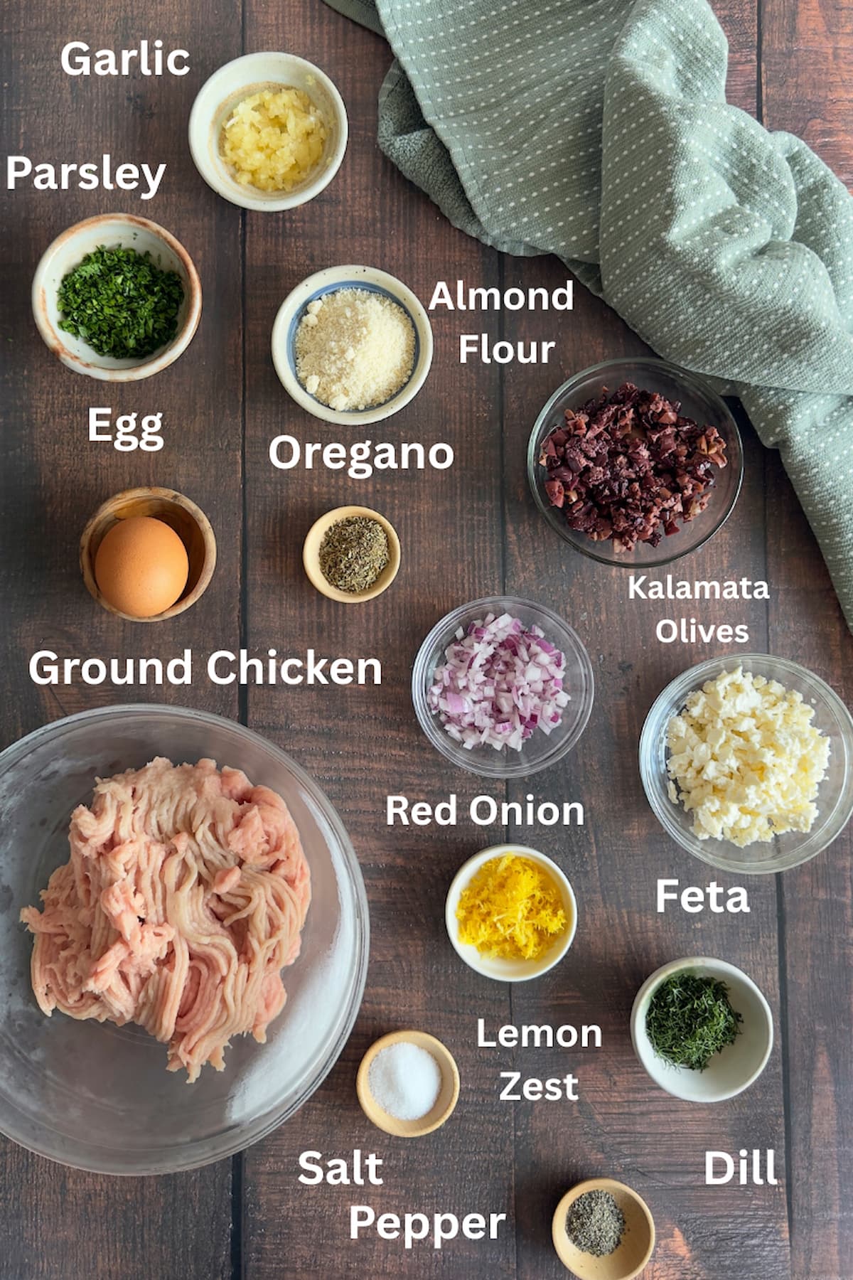 ingredients to make greek chicken meatballs laid out in small bowls - garlic, parsley, almond flour, egg, kalamata olives, oregano, dill, ground chicken, red onions, feta, lemon zest, salt, pepper.
