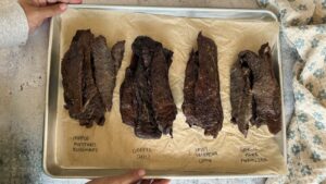 four different flavours of beef jerky on a parchment lined baking sheet.