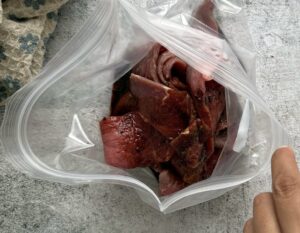 hand holding a ziploc bag open with pieces of marinated beef inside.