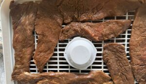 raw slices of marinated beef on a dehydrator tray.