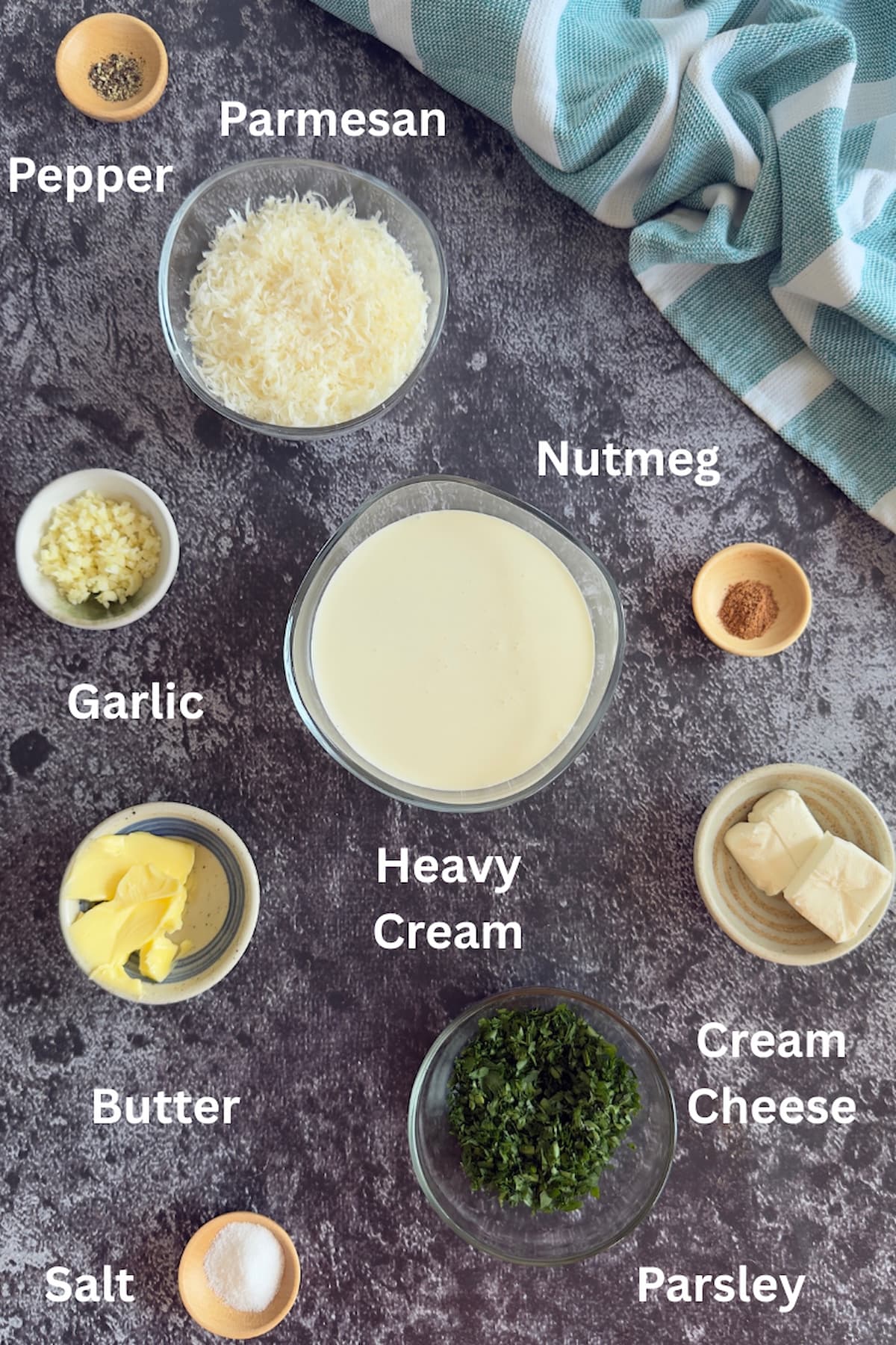 ingredients for low carb alfredo sauce laid out - pepper, parmesan, nutmeg, heavy cream, salt, parsley, butter, garlic, cream cheese.