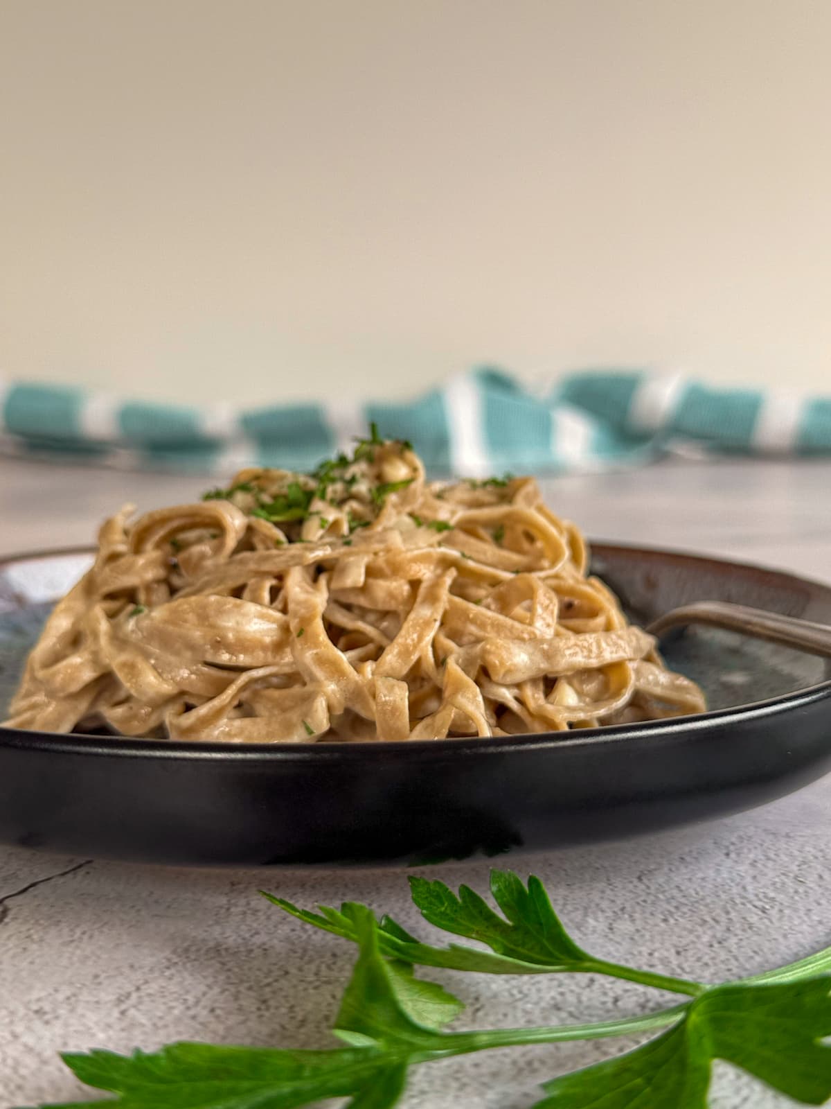 creamy low carb fettuccine alfredo piled high on a plate topped with fresh chopped parsley. Whole sprig of fresh parsley in front of the plate.