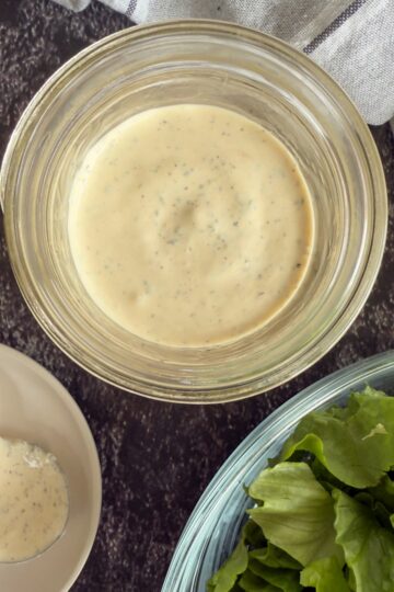 peppercorn ranch dressing in a jar next to a bowl of chopped romaine lettuce.