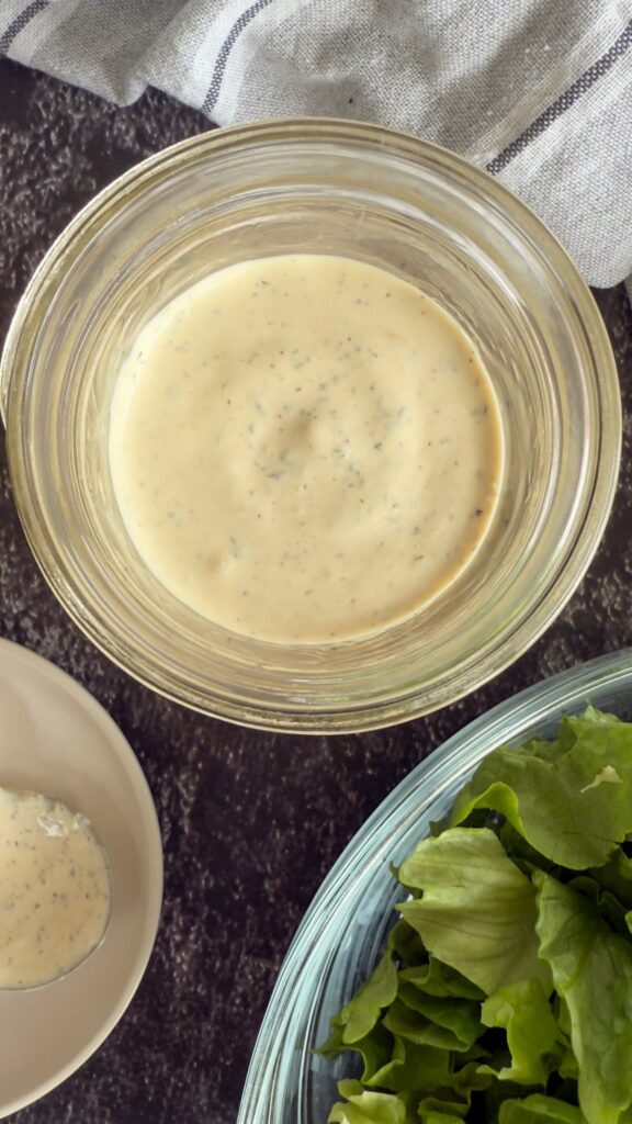 peppercorn ranch dressing in a jar next to a bowl of chopped romaine lettuce.