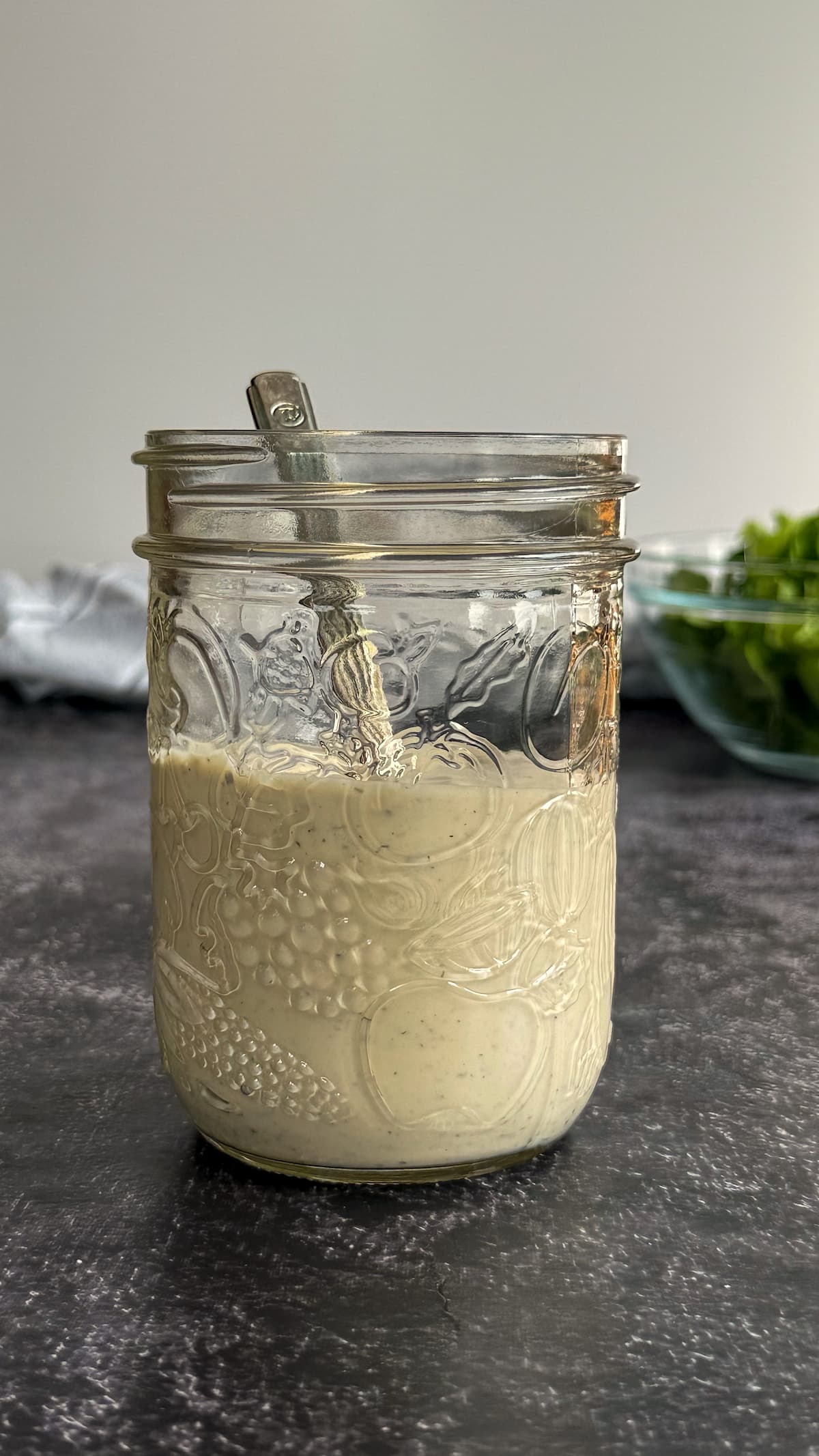 jar of peppercorn ranch dressing with a spoon in it, bowl of chopped romaine lettuce in the background.