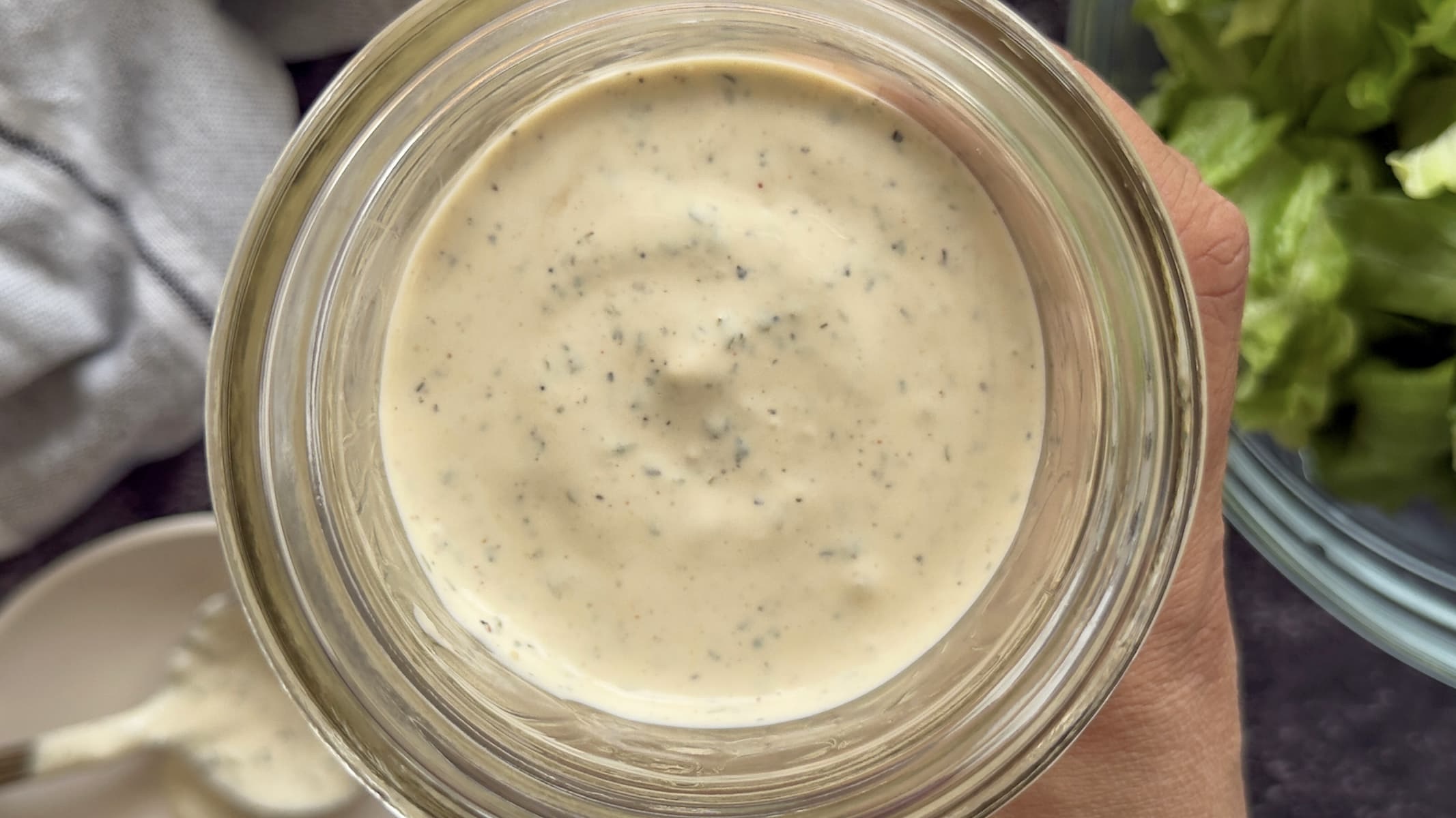 hand holding a jar of peppercorn ranch dressing over a bowl of chopped lettuce.