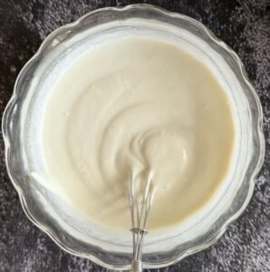creamy white sauce in a bowl with a little whisk.