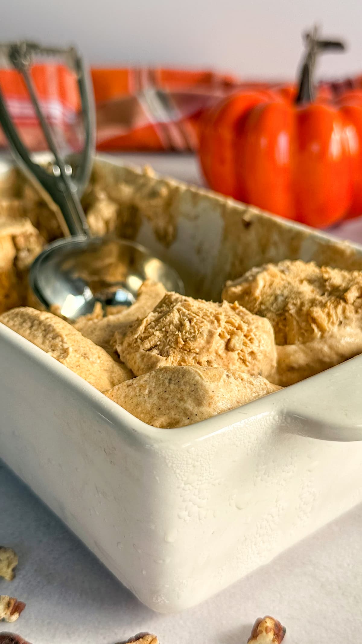 ice cream scoop in a container of pumpkin spice ice cream. pumpkin in the background.