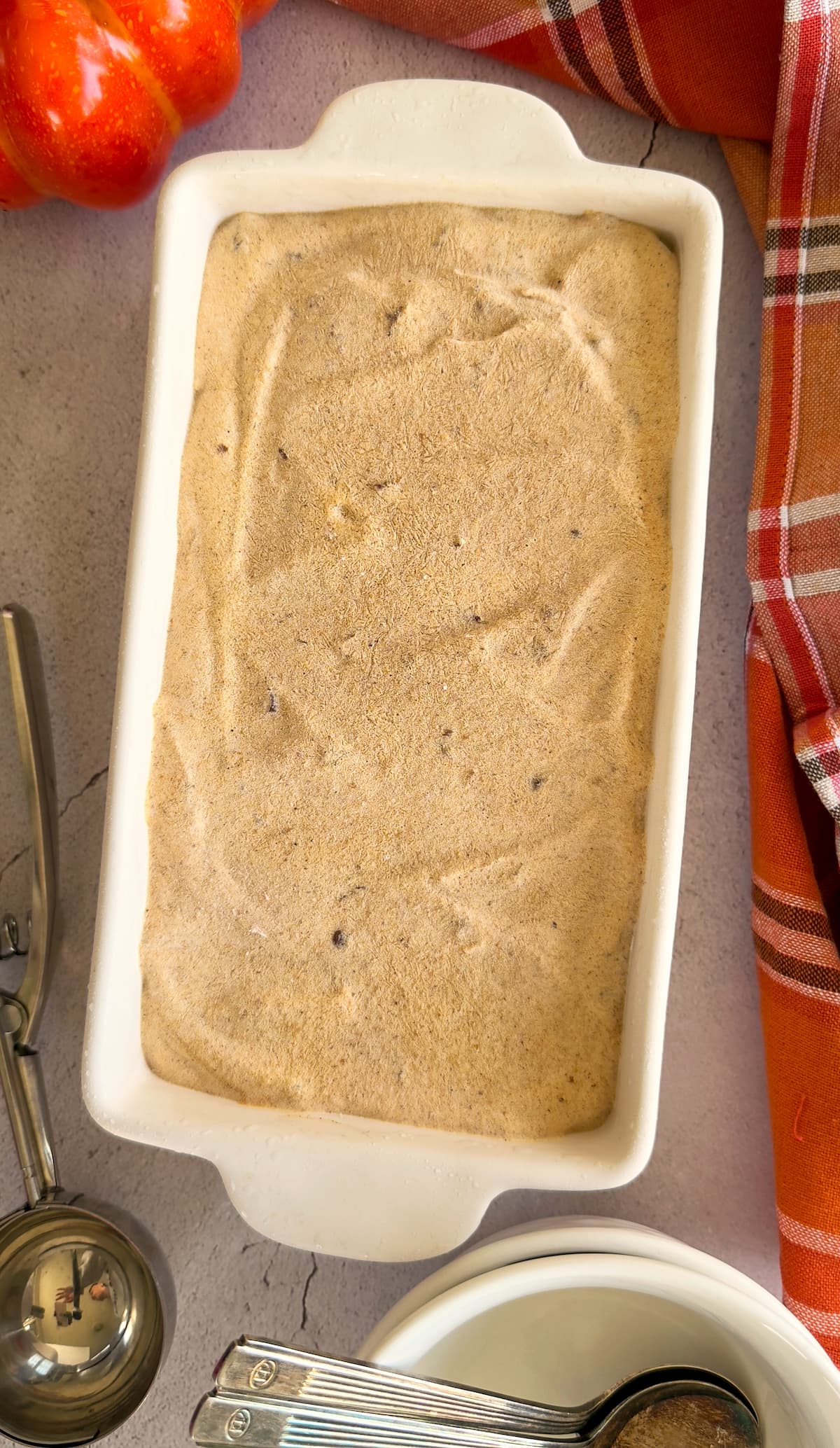 pumpkin spice ice cream in a rectangular baking dish. ice cream scoop and bowls with spoons around it.