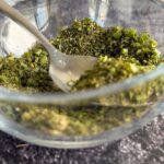 side view of a bowl of homemade ranch seasoning with a spoon in it. Dried chives scattered in the front.