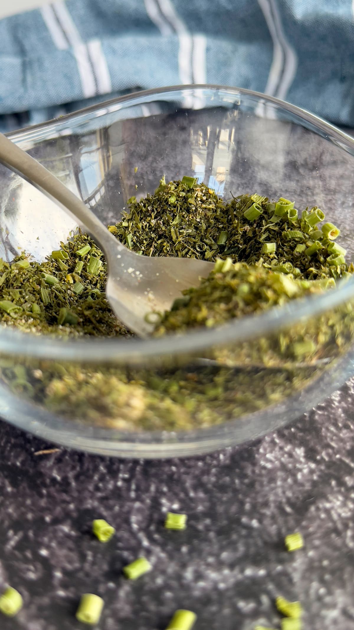 side view of a bowl of homemade ranch seasoning with a spoon in it. Dried chives scattered in the front.