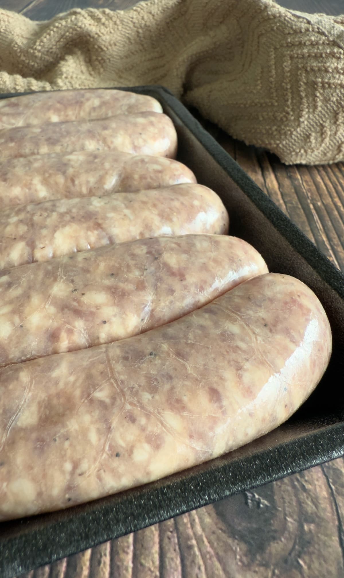 6 raw bratwurst sausage in a black tray.