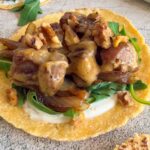 brie taco with chopped steak, arugula, walnuts, creamy white sauce, and caramelized onions. Another taco in the back and front.