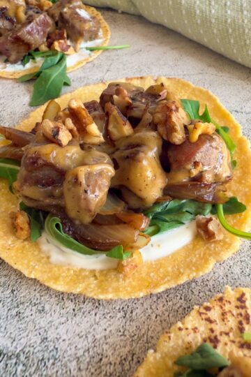 brie taco with chopped steak, arugula, walnuts, creamy white sauce, and caramelized onions. Another taco in the back and front.