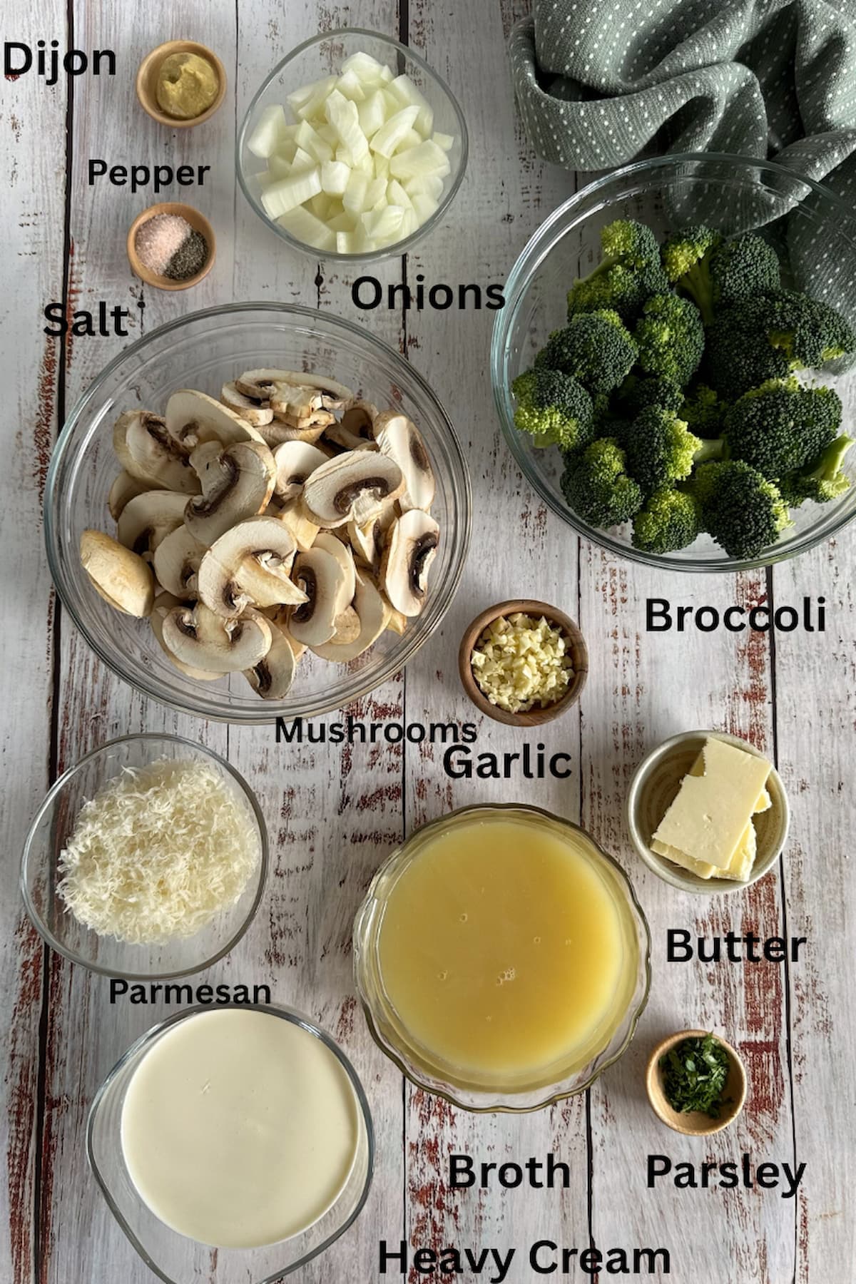 ingredients for broccoli mushroom soup laid out in separate bowls - dijon, salt, pepper, onions, broccoli, mushrooms, garlic, broth, butter, parmesan, heavy cream, parsley