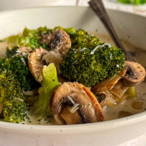 white bowl of broccoli and mushroom soup, spoon in the bowl, another bowl of soup in the background.