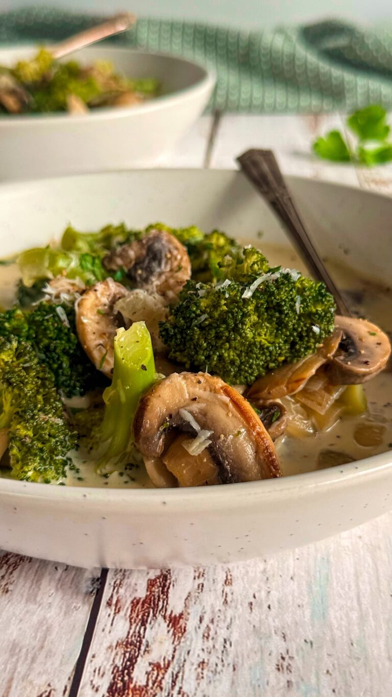 white bowl of broccoli and mushroom soup, spoon in the bowl, another bowl of soup in the background.