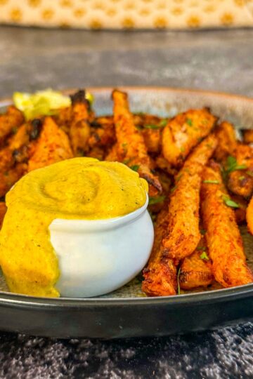curry mayo overflowing in a small white ramekin on a plate of jicama fries.