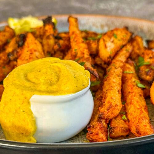 curry mayo overflowing in a small white ramekin on a plate of jicama fries.