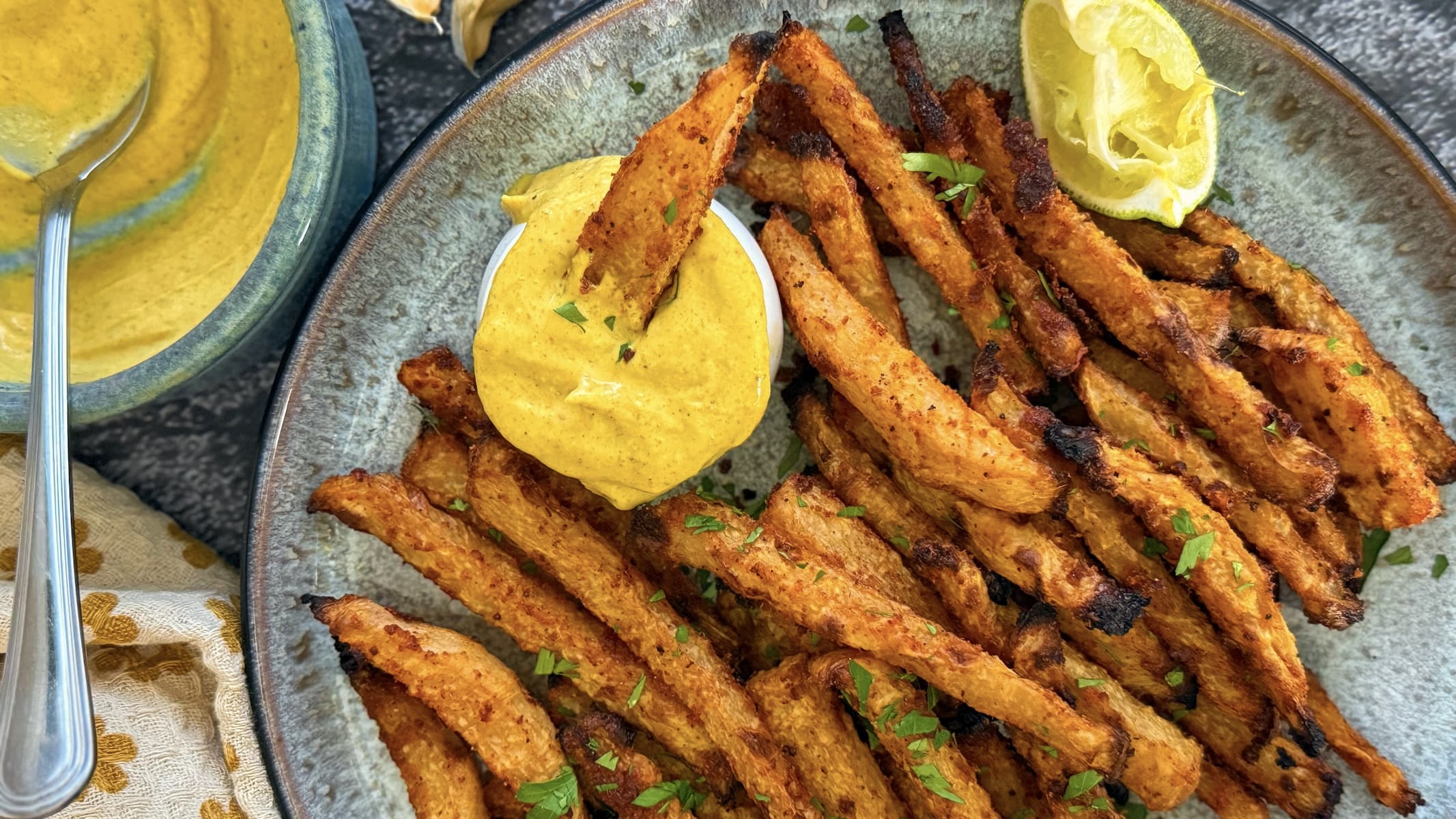 plate of jicama fries with fresh chopped parsley, a lime wedge, and a ramekin of curry mayonnaise. fry dipping into the mayo.