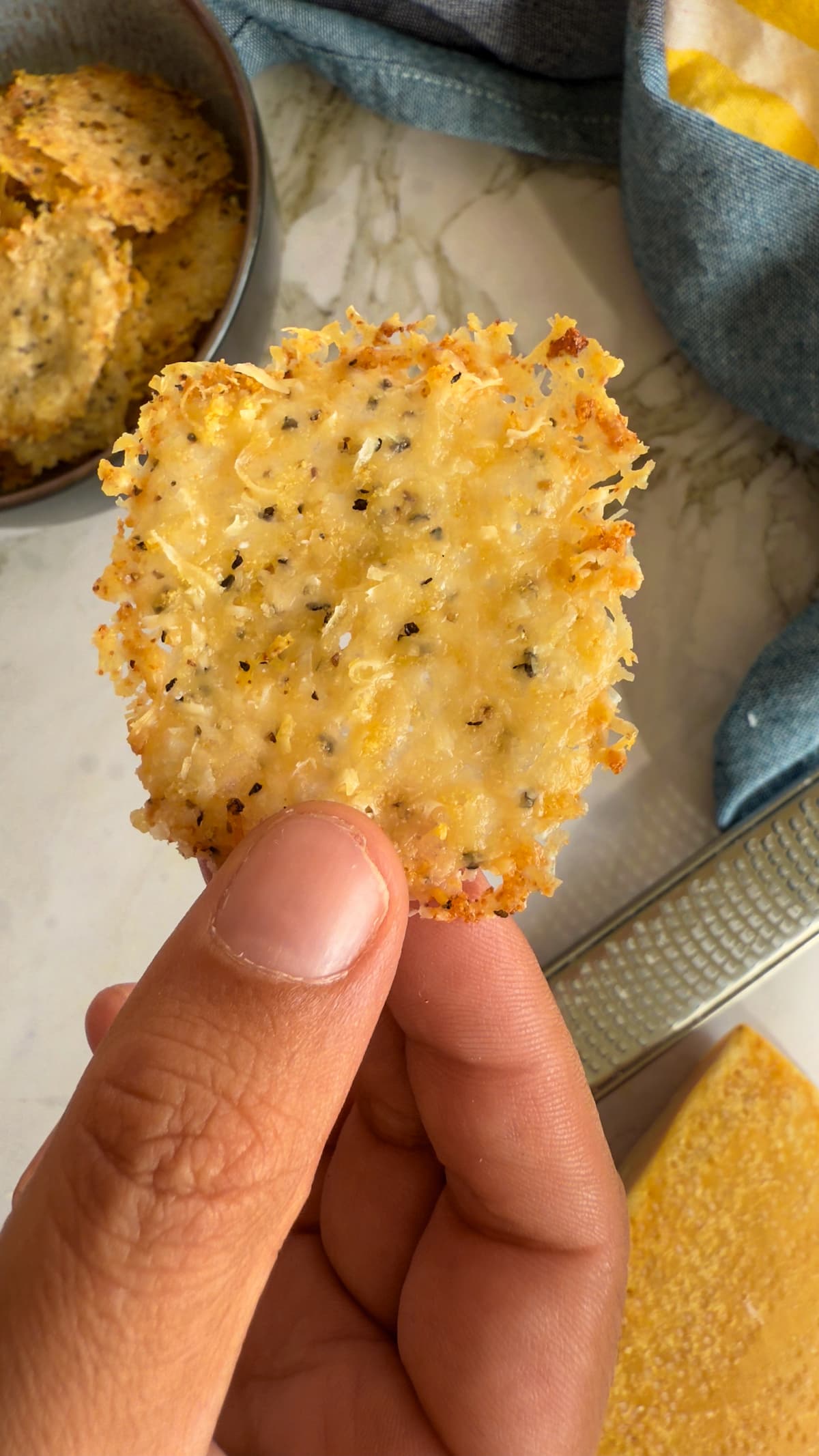 hand holding a parmesan chip over a bowl with more.