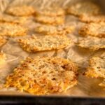 parmesan crisps spread out on a parchment lined baking sheet.