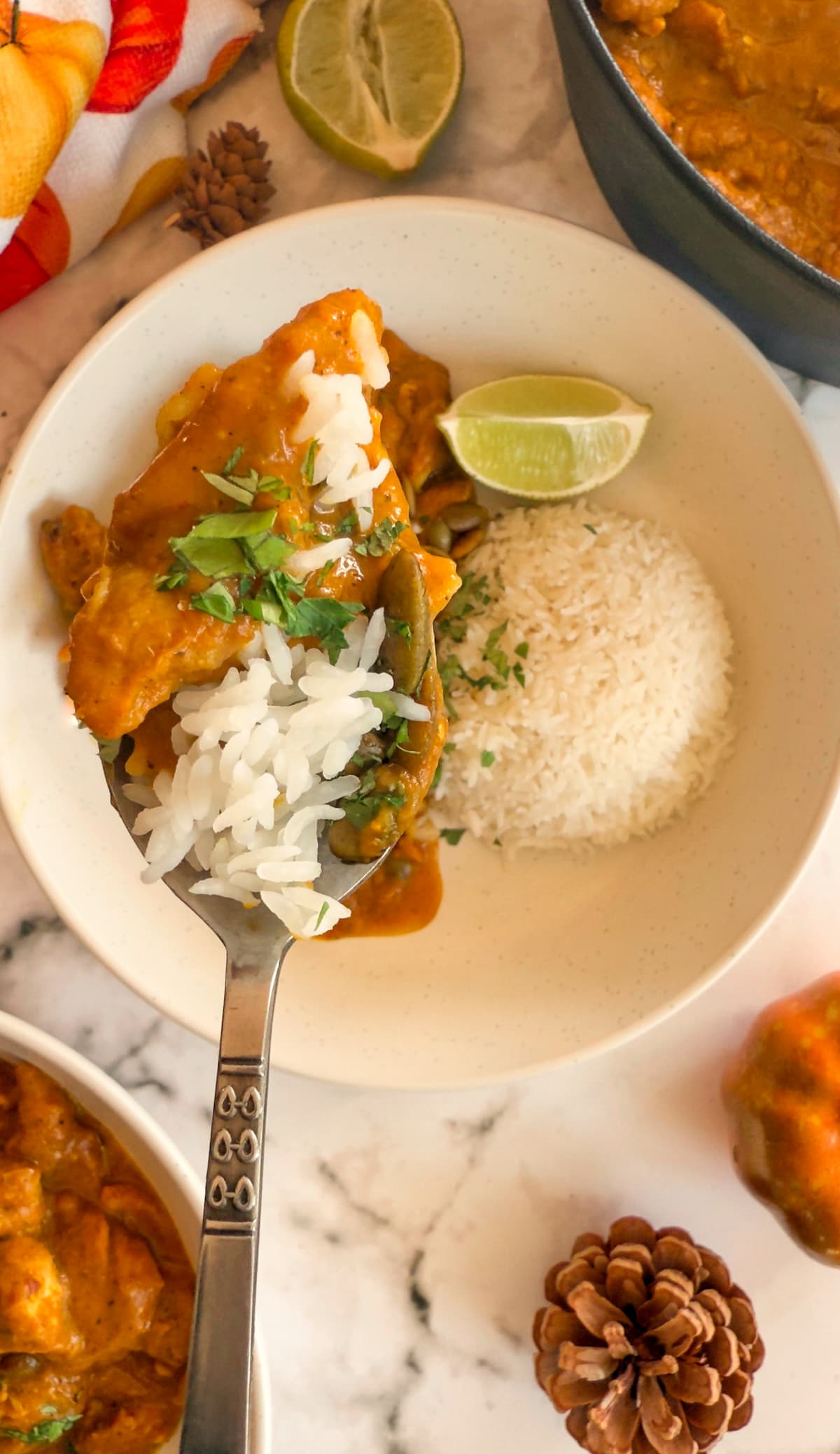 spoonful of rice and chicken pumpkin curry over a bowl with more, rice, and a lime wedge.