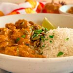 side view of pumpkin and chicken curry with rice, cilantro, pumpkin seeds, and lime juice.